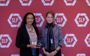 Two women smiling in front of a red backdrop.